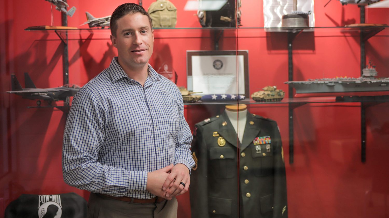 尼克·德雷克站在一个展示柜前，里面有几件军事文物和其他纪念品。