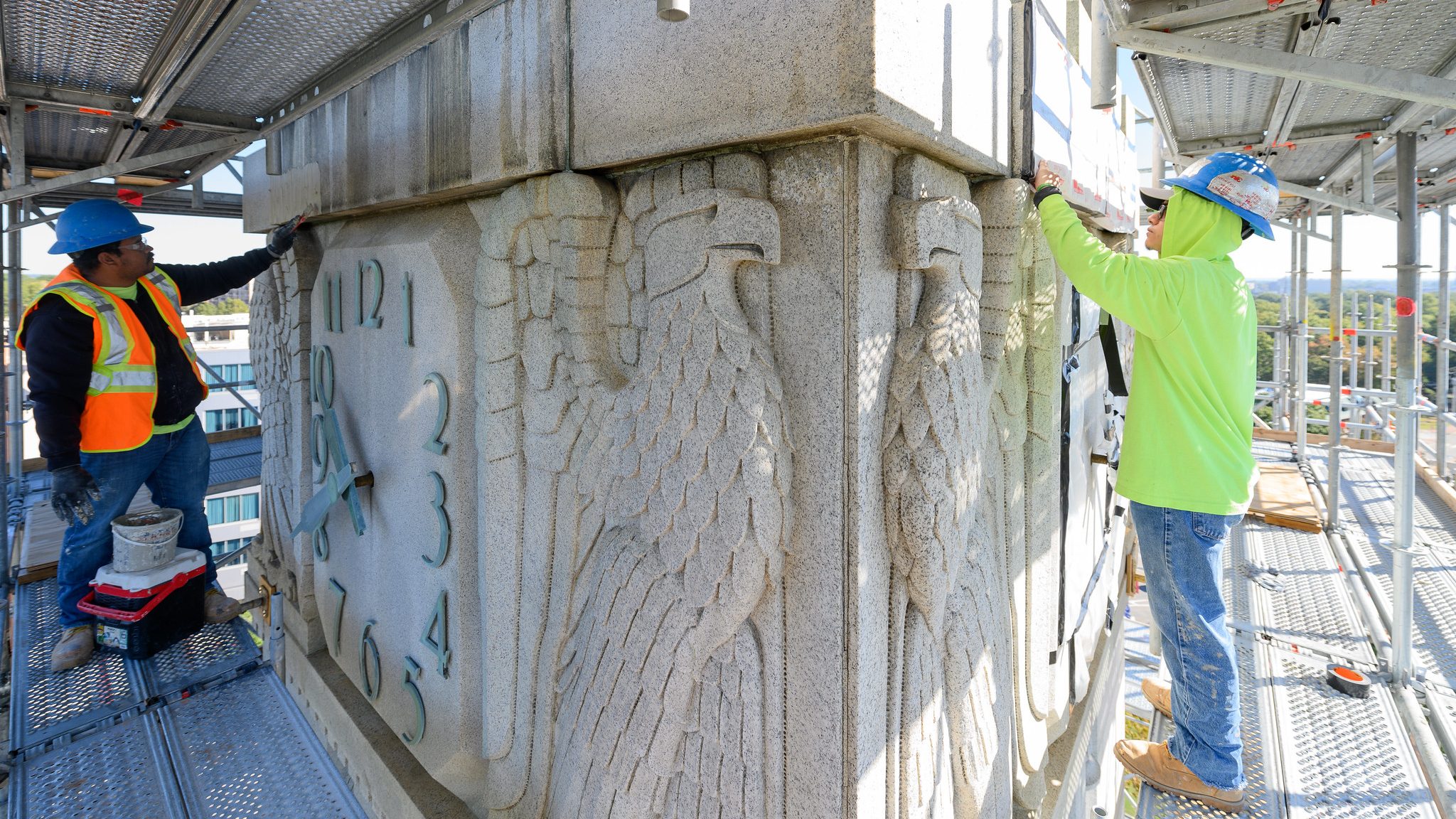 两名工人站在钟楼钟面和老鹰雕刻附近的脚手架上
