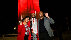 2021年北卡罗莱纳州毕业生站在前面red-illuminated纪念Belltower与他的父母。